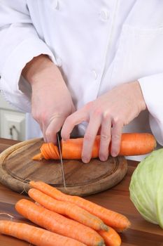 Chef preparing lunch and cutting carrot with knife