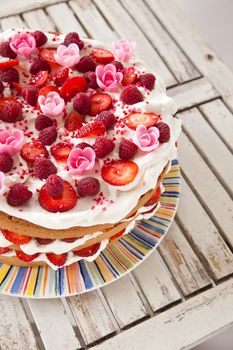 Delicious looking layered cake decorated with fruit, whipped cream and marizapan flowers