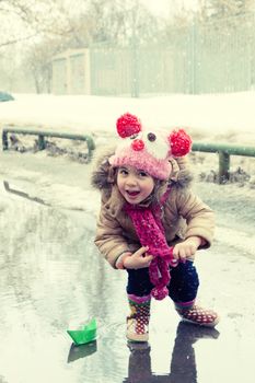 little girl plays with paper ships in a spring puddle