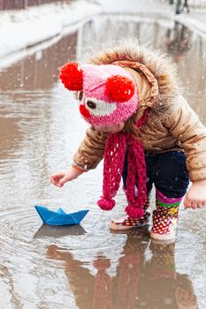 little girl plays with paper ships in a spring puddle