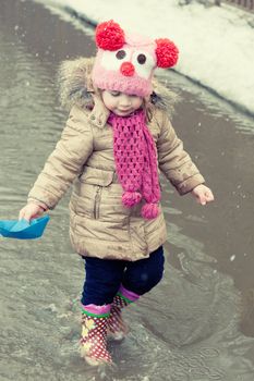 little girl plays with paper ships in a spring puddle