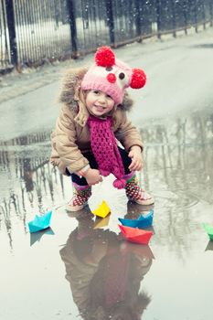 little girl plays with paper ships in a spring puddle