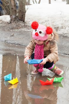 little girl plays with paper ships in a spring puddle