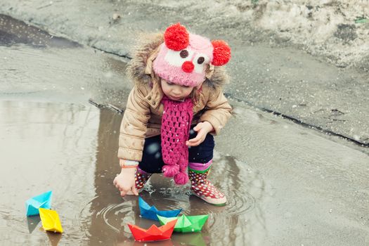 little girl plays with paper ships in a spring puddle