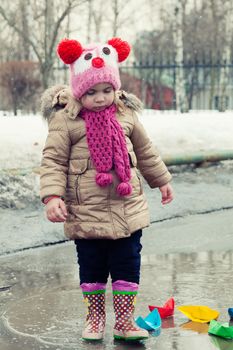 little girl plays with paper ships in a spring puddle