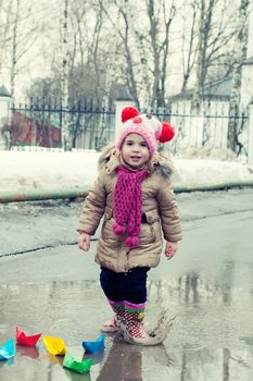 little girl plays with paper ships in a spring puddle