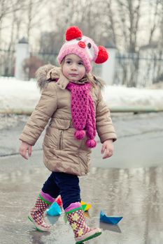 little girl plays with paper ships in a spring puddle