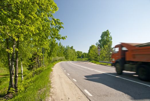 Dirt road with asphalt dump truck in motion