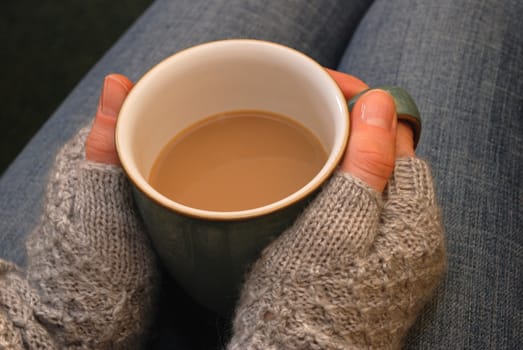 A woman in a warm jumper holding a cup of tea or coffee on her lap