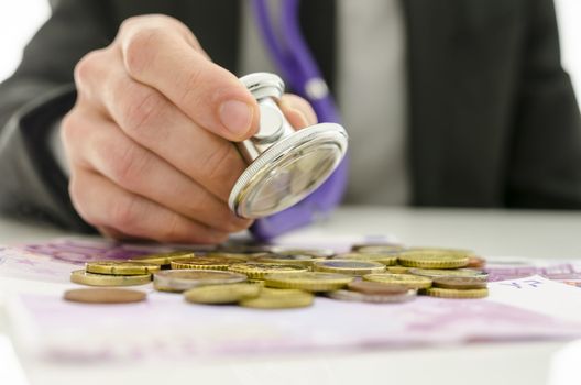 Closeup of businessman checking Euro coins and banknotes with stethoscope. Concept of financial crisis solution.