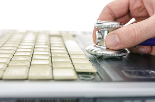 Male hand holding stethoscope on keyboard of an old and dirty laptop. Shallow dof.