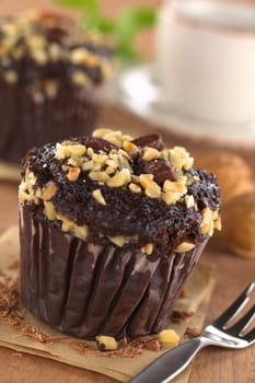 Chocolate-walnut muffins with coffee cup in the back (Selective Focus, Focus on the first chocolate piece on the muffin) 