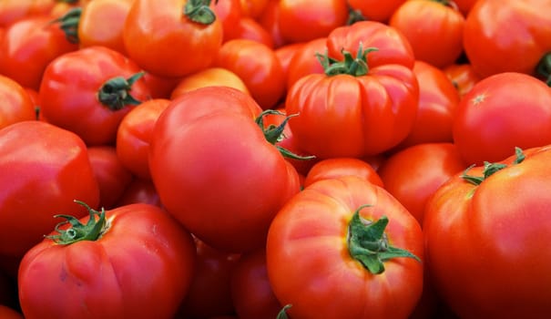 Pile of ripe red tomatoes with green tops and soft focus background