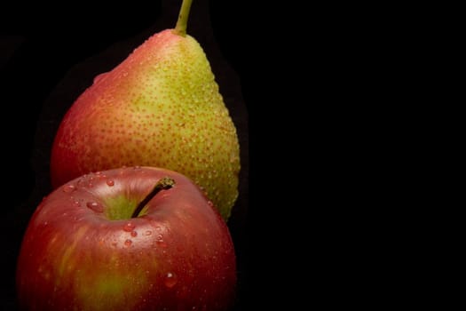 A juicy apple and pear with water drops on black