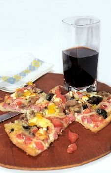 Parts of cutting pizza with ham and vegetables and dark drink glass 