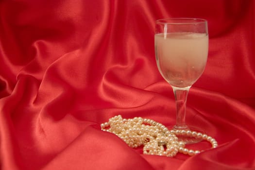 A glass of champange and a pile of pearls, on red silk