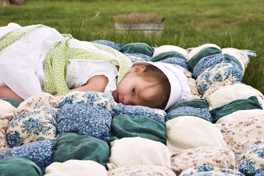 Amish child lying outdoors on a handmade biscuit quilt.