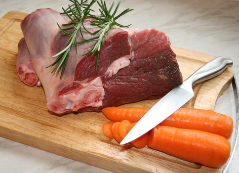 A joint of lamb ready for cooking,with carrots and rosemary