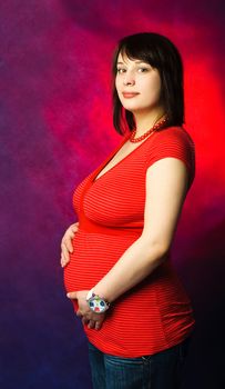 studio portrait of a beautiful young pregnant woman against red background