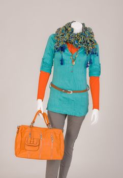 Mannequin dressed with a scarf, T-shirt, beige pants and orange bag