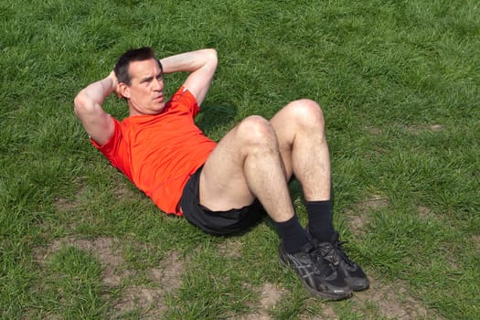 Middle Age Man Exercising doing Situps on the Grass in the Sunshine