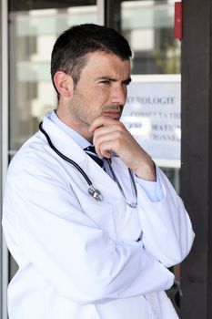 pensive doctor with stethoscope in front of hospital