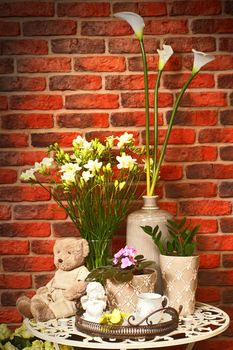 Some porcelain dolls and teddy bears on a table against a wall from a red brick