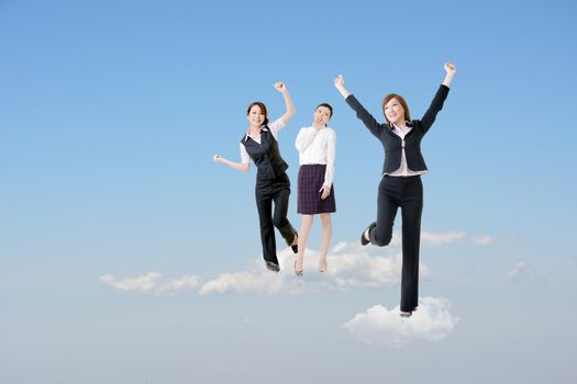 Cheerful three Asian business women stand on clouds and raise their arms feel freedom and exciting over blue sky.