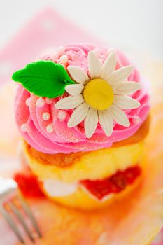 A two layer cupcake with pink and white buttercream sugar flower and gold powder on a white background as a studio shoot