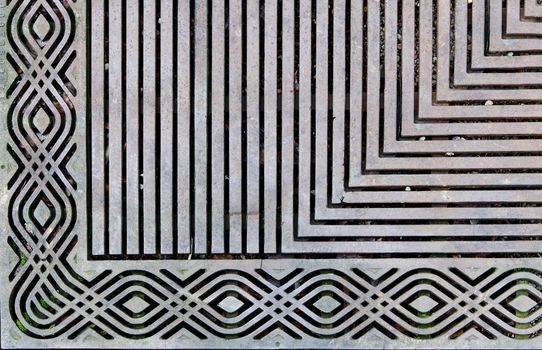 Corner of an ornately designed steek grating on the sidewalk