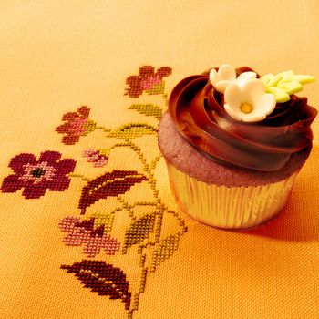 beautiful cupcake decorated with chocolate and flowers on vintage tablecloth