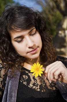 View of a beautiful girl on a urban park with a yellow flower.