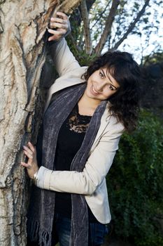 View of a beautiful girl on a urban park peeks behind the tree.