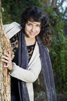 View of a beautiful girl on a urban park peeks behind the tree.