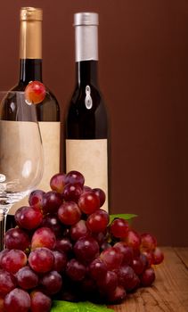 red grapes with wine bottles on brown background