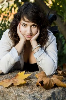 Beautiful young girl lies down on a stone rock on a urban park.