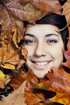 Close view of the face of a beautiful girl surrounded by autumn leaves.