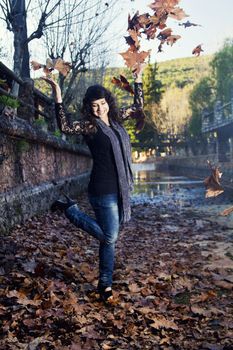 Beautiful girl throws in the air a bunch of autumn leaves.