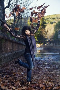 Beautiful girl throws in the air a bunch of autumn leaves.