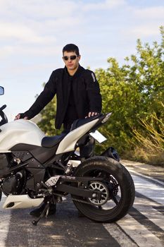 View of a man with a motorcycle on a asphalt road.