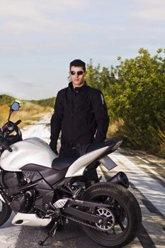View of a man with a motorcycle on a asphalt road.