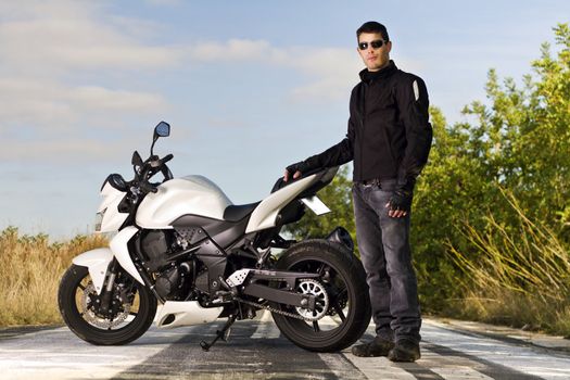View of a man with a motorcycle on a asphalt road.