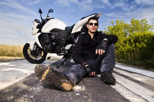 View of a man with a motorcycle on a asphalt road.