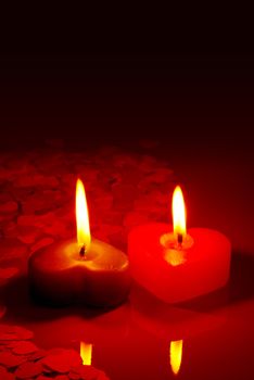 Two burning heart shaped candle on a red table