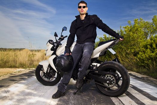 View of a man with a motorcycle on a asphalt road.