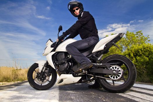 View of a man with a motorcycle on a asphalt road.