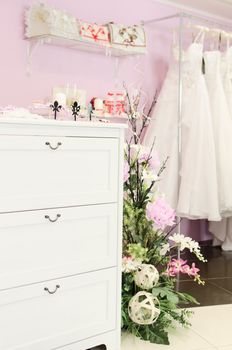 Wedding store background. White bridal dresses. Artificial flowers and different stuff on glass shelfs