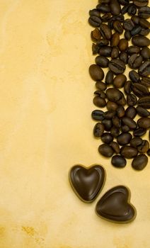 Two heart shaped chocolate candies and coffee beans on grungy paper