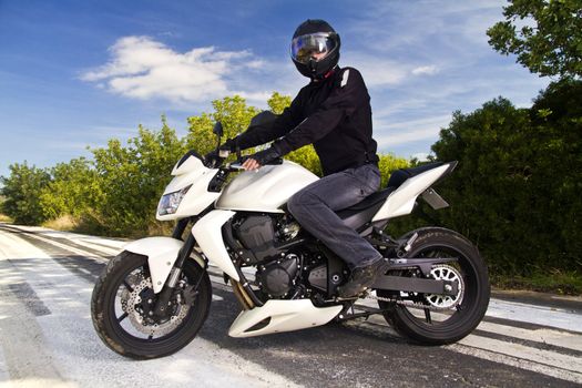 View of a man with a motorcycle on a asphalt road.