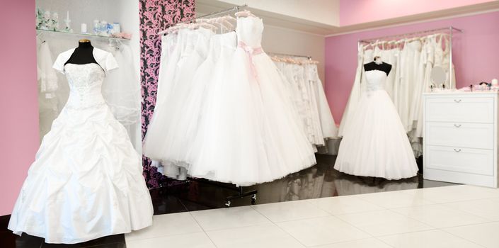 Wedding store panorama. Shallow depth of field. White bridal dresses. Artificial flowers and different stuff on glass shelfs